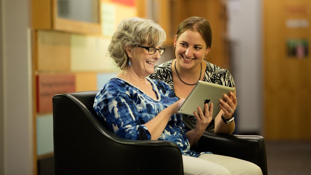 A student helping an older woman use a tablet