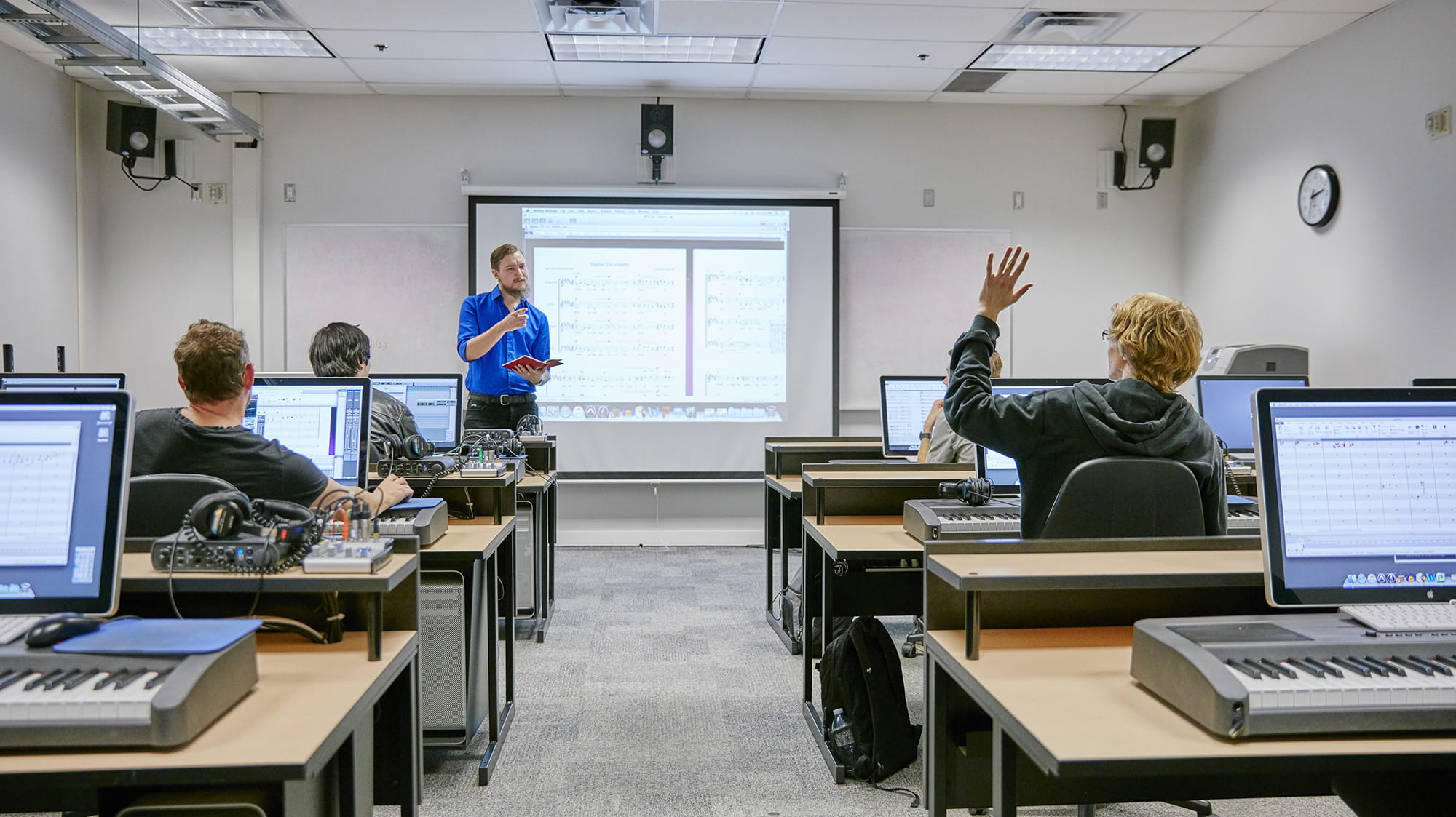 An instructor talking to students who are at computers with music keyboards