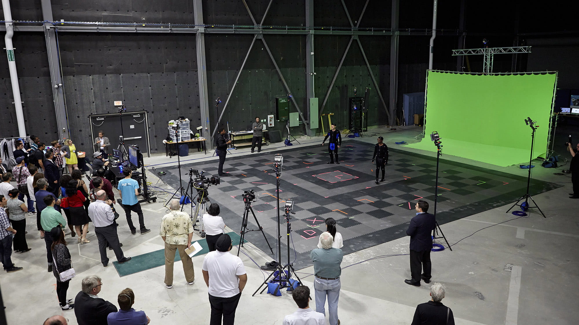 A large studio filled with a production crew, cameras, lights, and a green screen