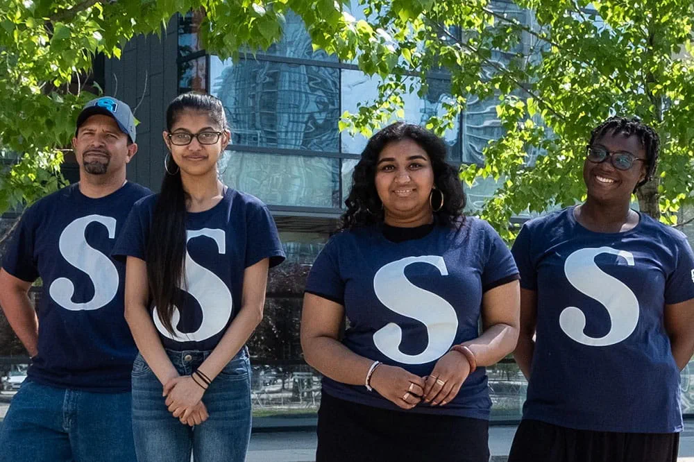 Four Sheridan students standing side-by-side in their 'S' t-shirts