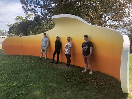 students pose in front of embrace sculpture