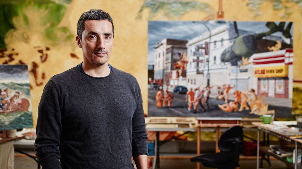 Kent Monkman standing next to a painting in a studio