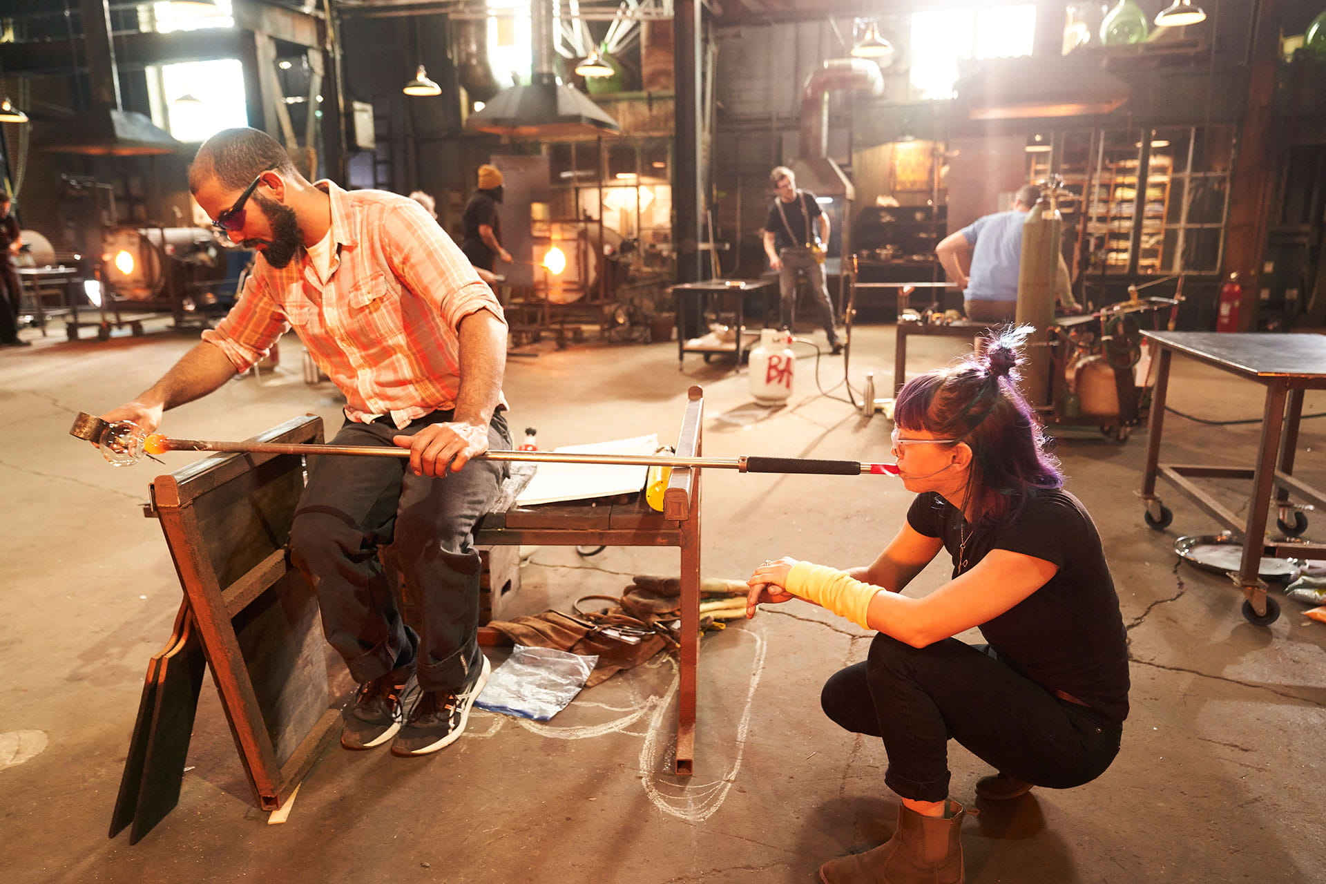Two glassblowers working with glass on the set of Netflix's Blown Away