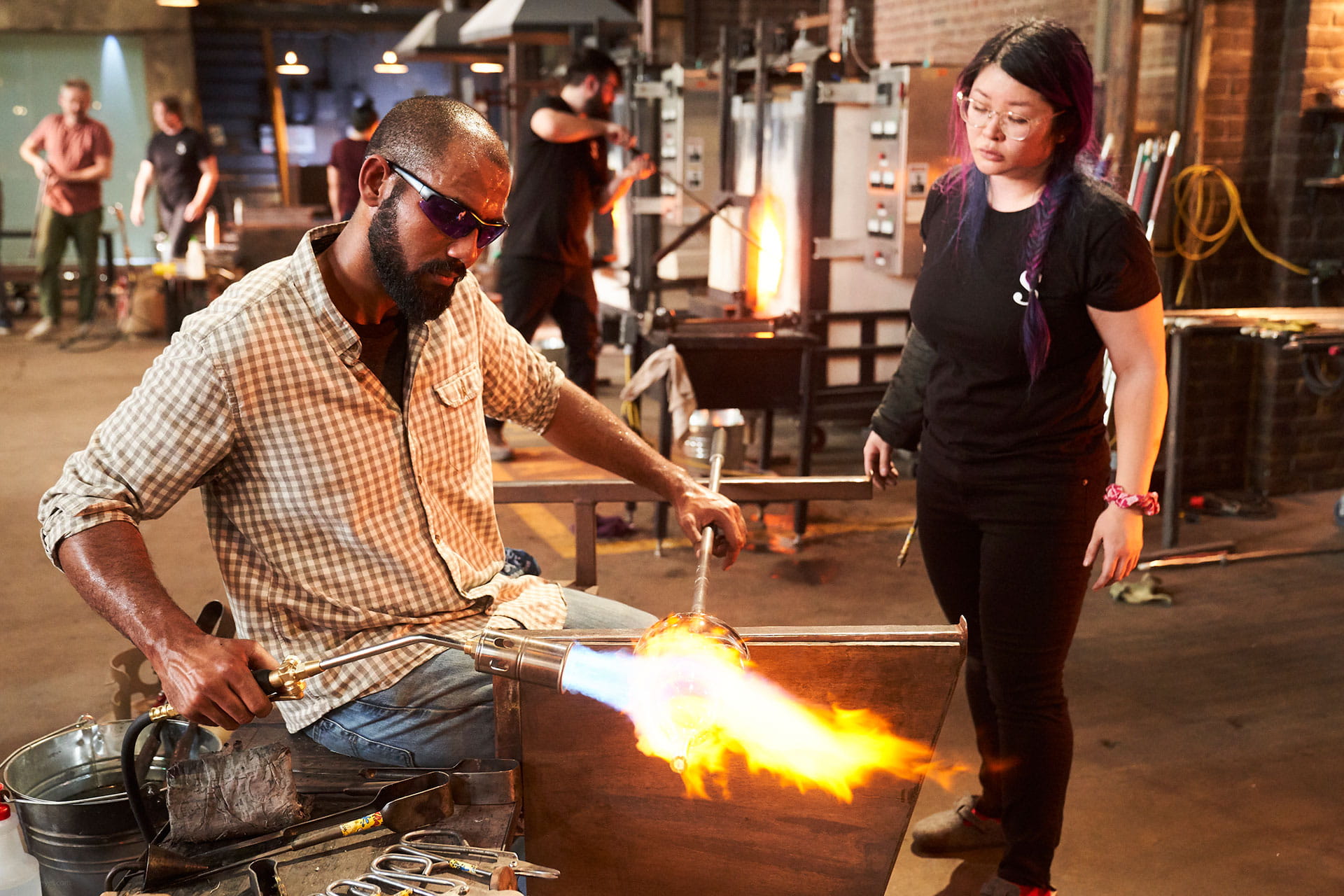 Two glassblowers working with glass on the set of Netflix's Blown Away