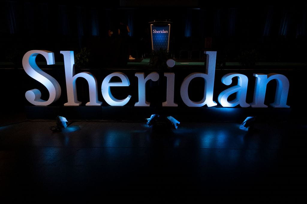 Large letters on a stage spell out 'Sheridan' with a podium sitting behind them.