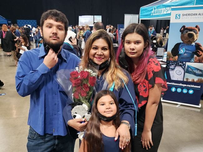 Meena Chowdhury holding flowers and posing for a photo with her three children at her convocation ceremony.