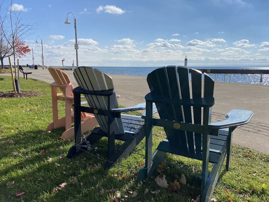 The back of three Muskoka chairs set up side-by-side facing the beach.