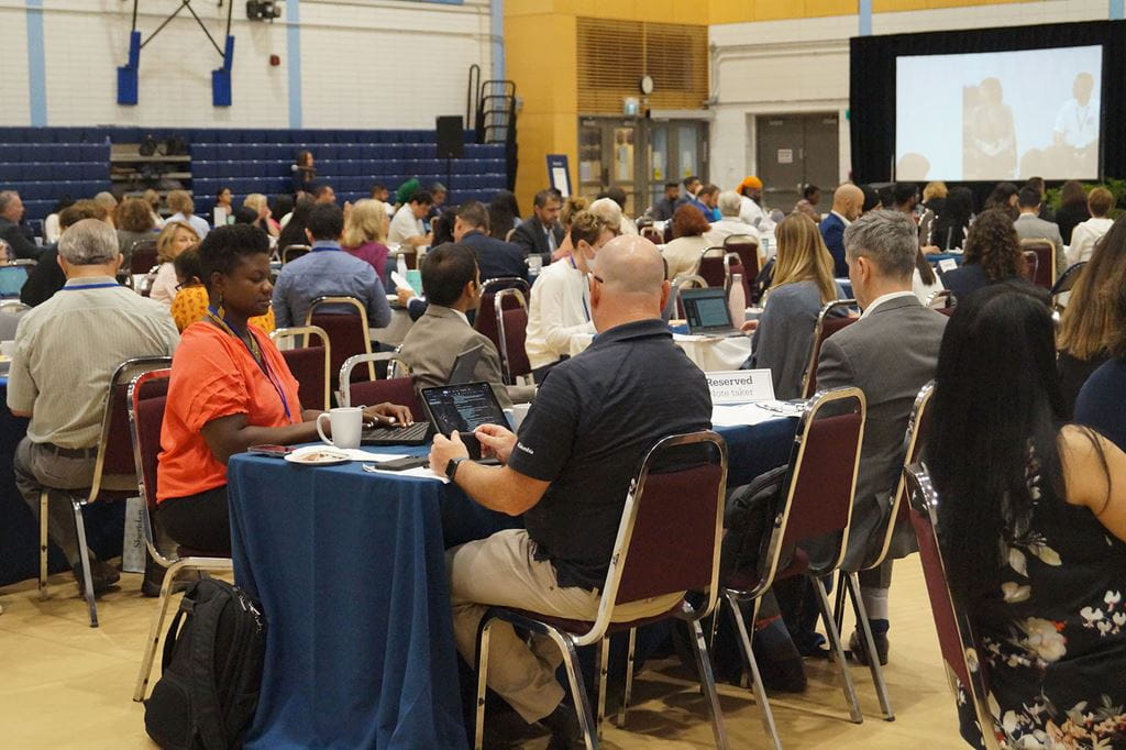 Summit attendees seated at tables in a gymnasium.