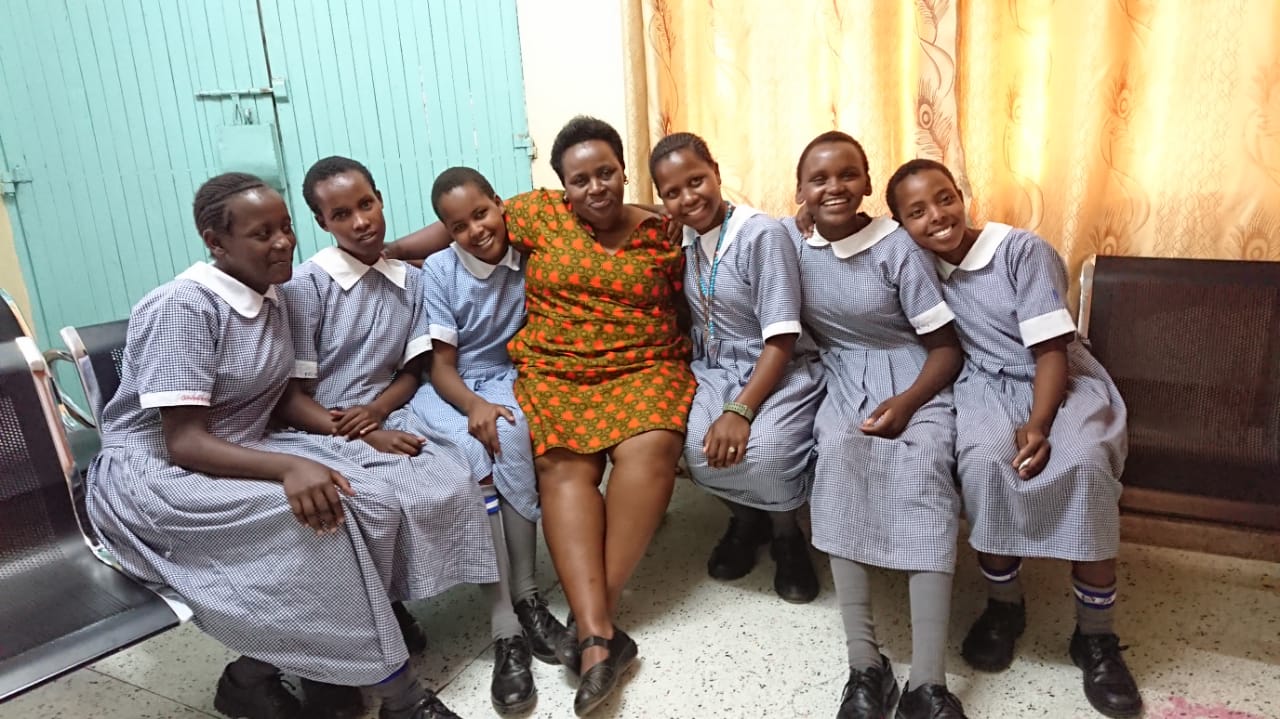 Sheridan VP, Inclusive Communities Dr. Jane Ngobia sits on a bench with six Kenyan children