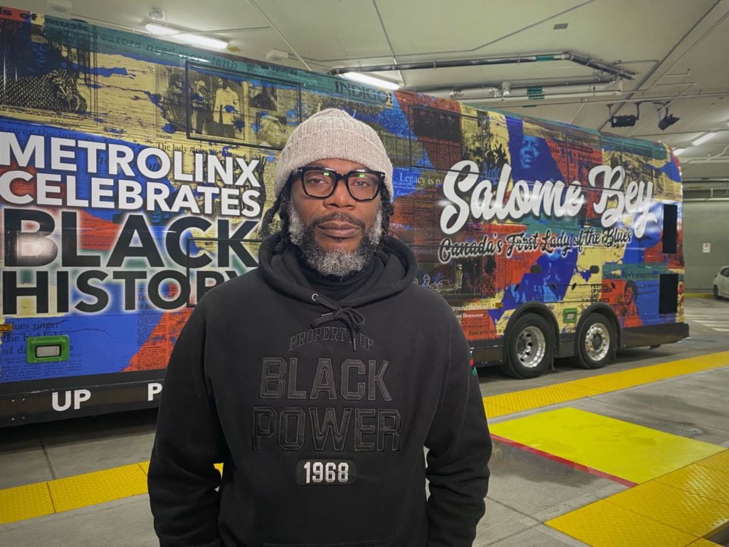 Mark Stoddart standing in front of the GO bus with his design featuring musician Salome Bey, in celebration of Black History Month.