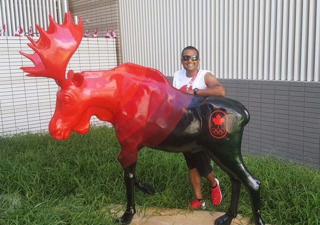 Alumnus Surinder Budwal standing behind Canada's moose statue at the Tokyo 2020 Olympic Games.