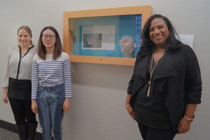 Dr. Lia Tsotsos, Laura Yang and Sirena Liladrie standing outside of a showcase with Yang's Conceptual Design project