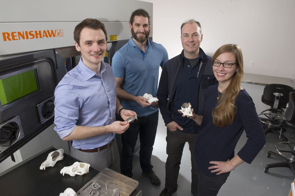 Team of researchers standing in front of an industrial 3D printer
