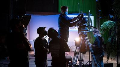 A person sets up a camera shot in studio while others observe.