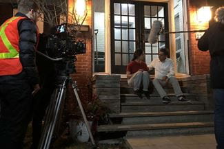 Filming a scene of a man and woman having a discussion while sitting on the steps in front of a building.