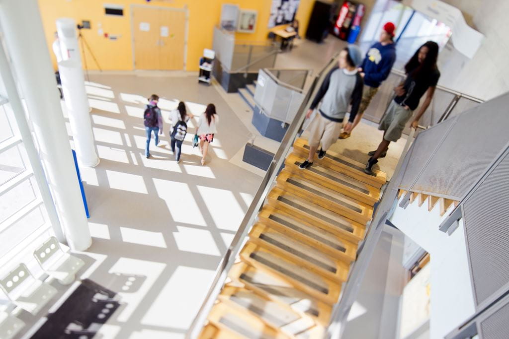 Students in the hallway and walking down stairs in the bright J wing of Sheridan's Trafalgar Campus