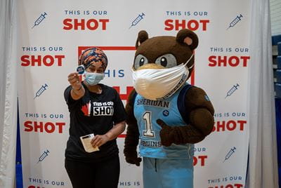 Sheridan's mascot with a vaccine clinic attendee posing in front of a 'This is your shot' backdrop