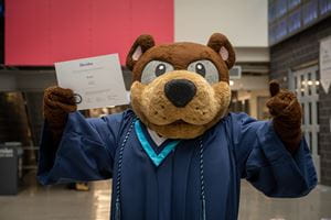 Bruno mascot in graduation gown, with diploma