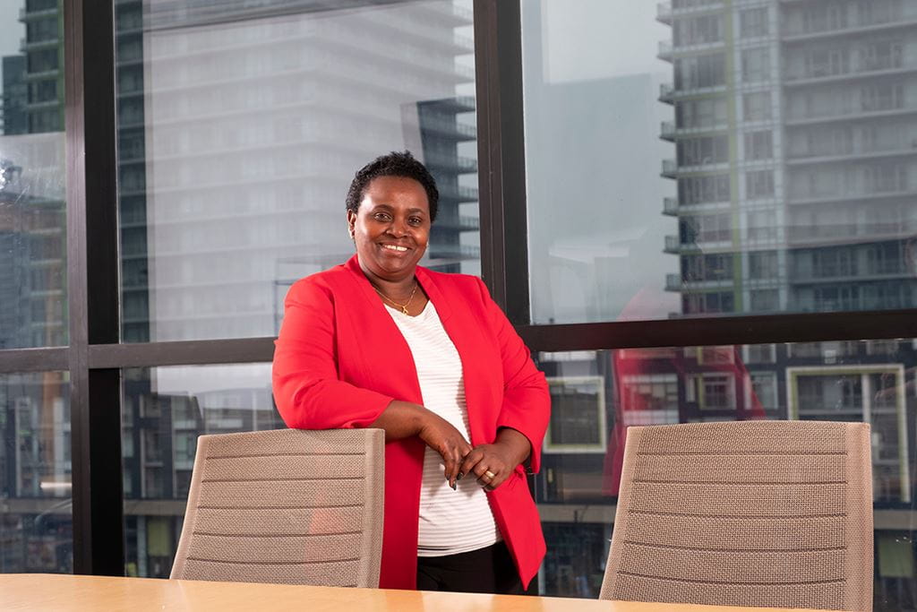 Dr. Jane Ngobia, Sheridan's Vice President of Inclusive Communities, smiling and standing behind a chair around a boardroom table