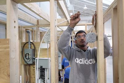 A student feeds electrical wire through a framed wall in Sheridan's electrical lab