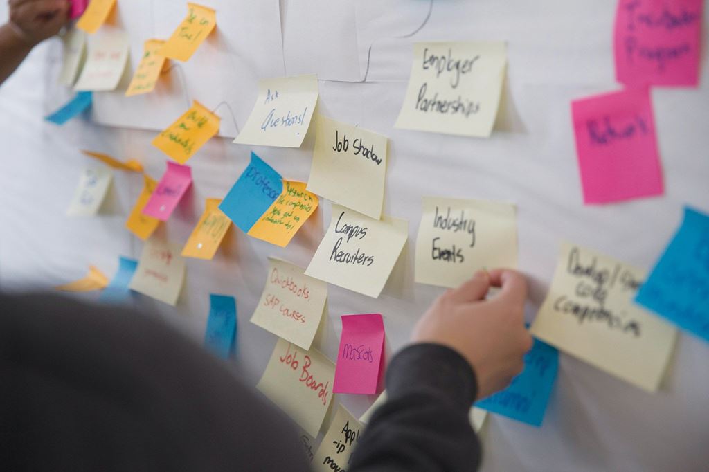 A person puts sticky notes on the wall during a brainstorming exercise.