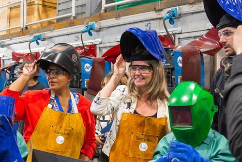 Ontario Associate Minister of Women's Social Economic Opportunities Charmaine Williams and Minister of Colleges and Universities Jill Dunlop lift up their welding masks during a demonstration in Sheridan's welding lab