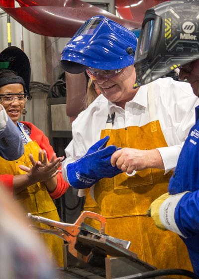 Ontario Premier Doug Ford wears a welding mask and gloves in Sheridan's lab