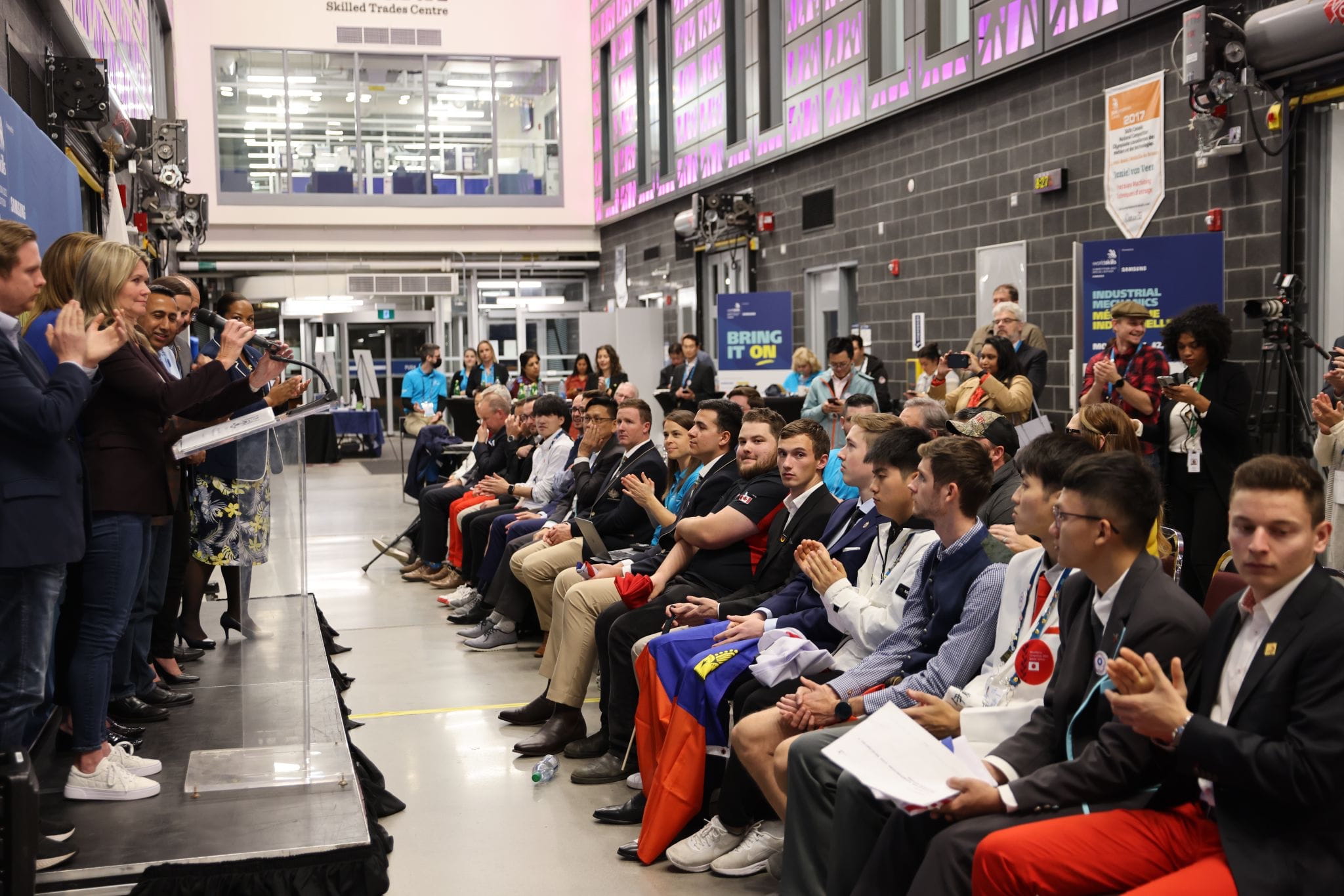 Various Ontario Members of Provincial Parliament stand in front of competitors and others during the opening ceremonies of the WorldSkills Competition 2022 Special Edition's Industrial Mechanics event.