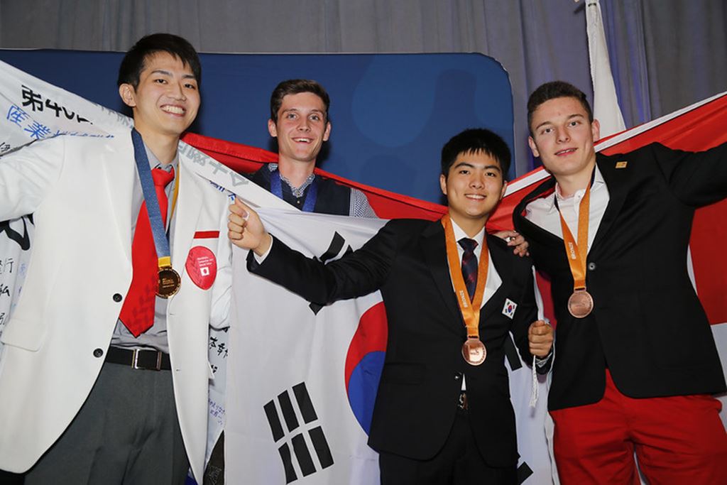 Medal winners from the WorldSkills Competition 2022 Special Edition's Industrial Mechanics event stand side by side displaying the flags of their home countries.