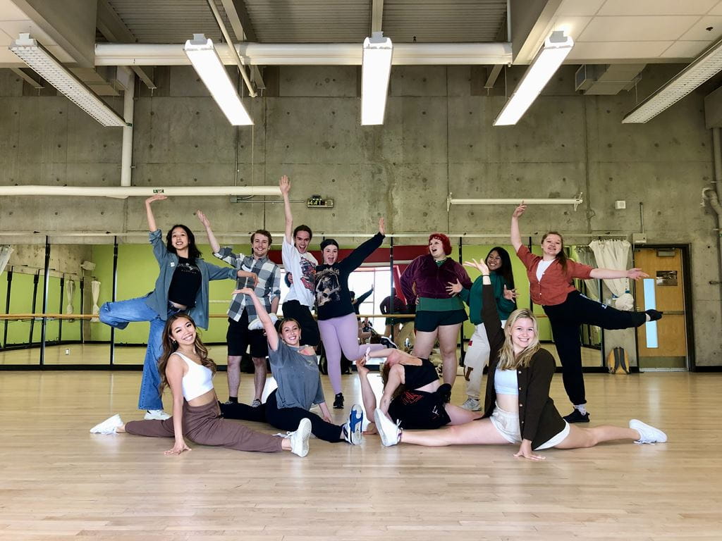 A group of music theatre student counsellors pose on a dance studio floor